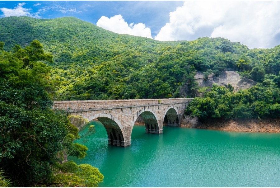A footpath that connects the banks of one of the reservoirs in Tai Tam Country Park. There is greenery all around and the water in the reservoir is a beautiful shade of turquoise.