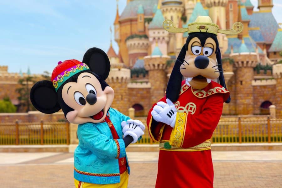mickey mouse and goofy in festive outfits pose in front of disneyland castle