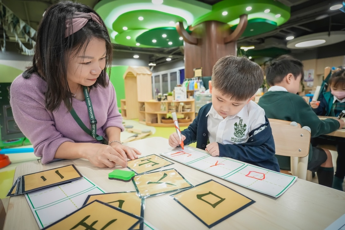 a teacher sitting with a child supervising chinese writing