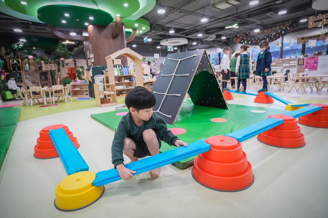 a child setting up play equipment in a play area surrounded by open classrooms