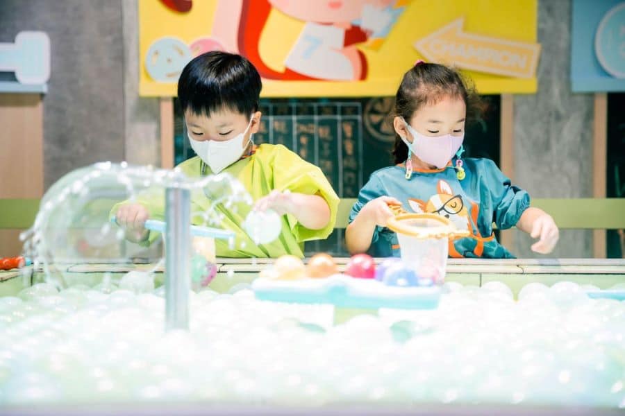 Two children at Mr. Tree at the mini fishing pool. They are using the nets in their hands to fish out colourful plastic balls from the pool.