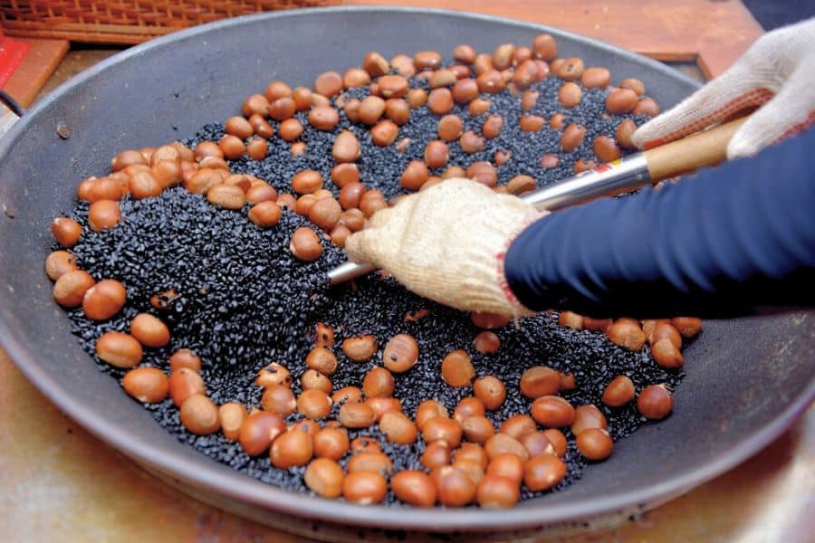 a person roasting chestnuts in a large iron wok with quartz sand and sugar