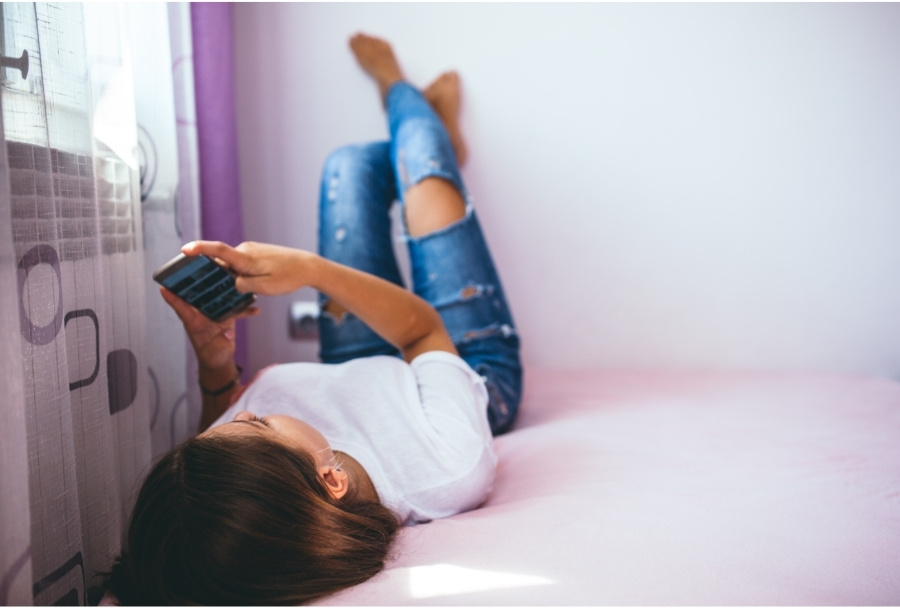 teenager using smartphone while lying on bed