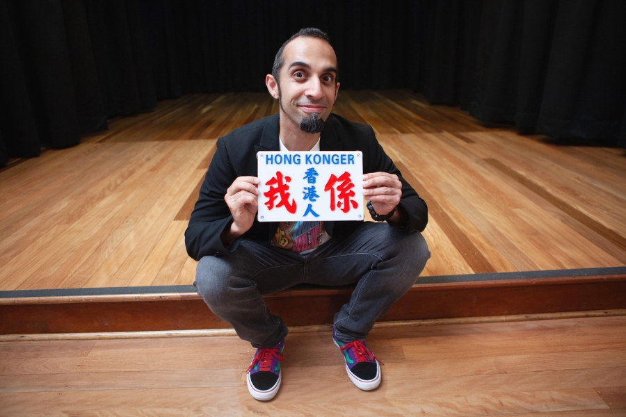 stand up comedian vivek mahbubani  posing with a sign saying hong konger